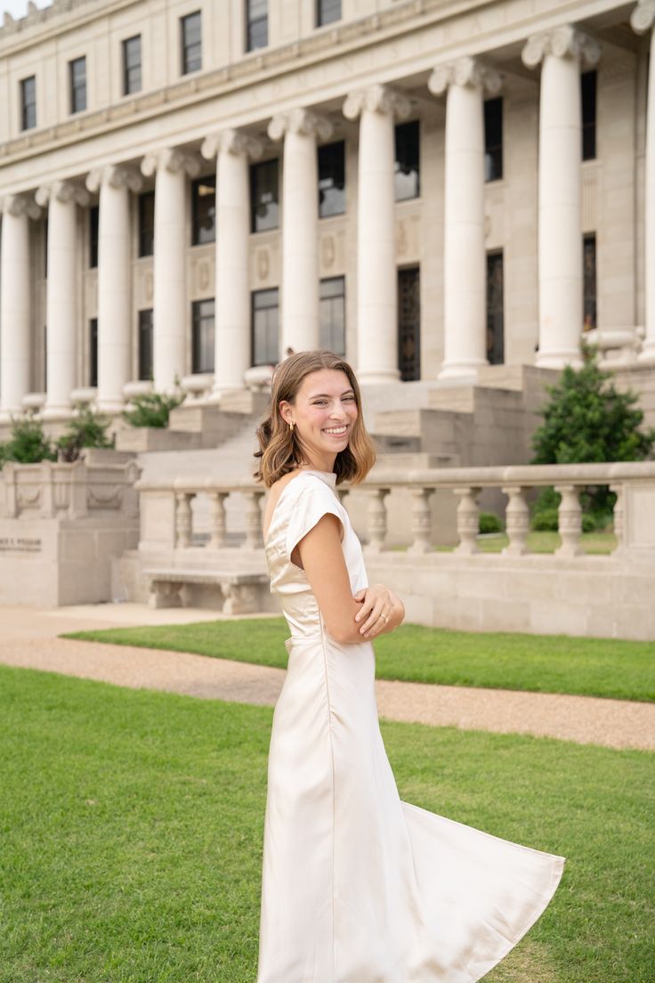 a woman standing in front of a building wearing a white dress and smiling at the camera