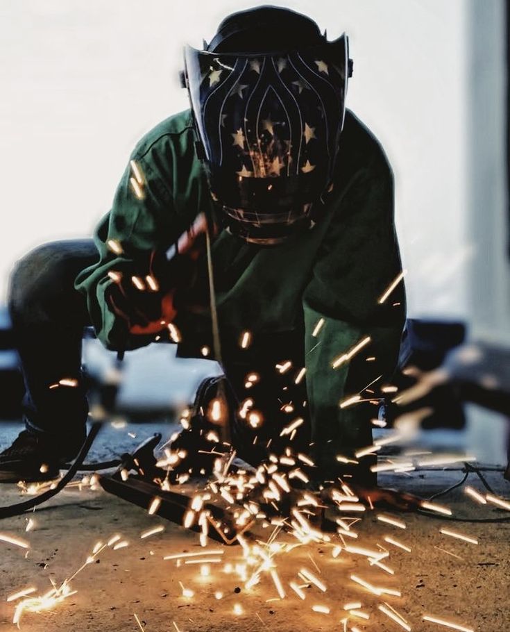 welder in protective gear working with sparks on the ground and wearing a gas mask