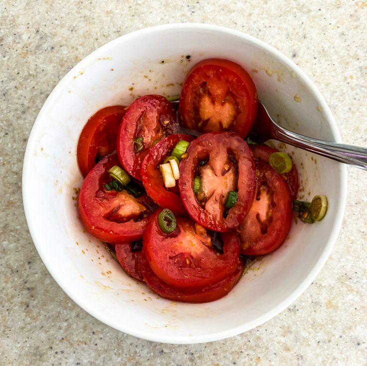 a white bowl filled with sliced tomatoes on top of a marble counter next to a spoon