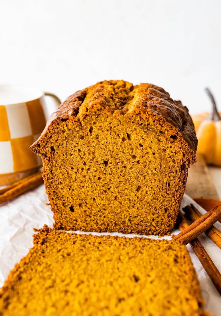 two slices of pumpkin bread sitting on top of a table next to cinnamon sticks and an orange mug