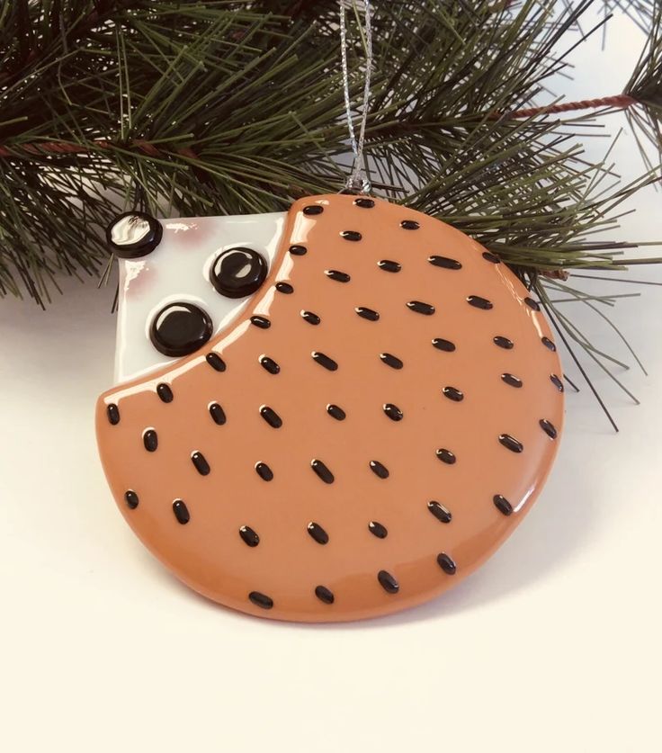 a ceramic ornament hanging from a pine tree with some black dots on it