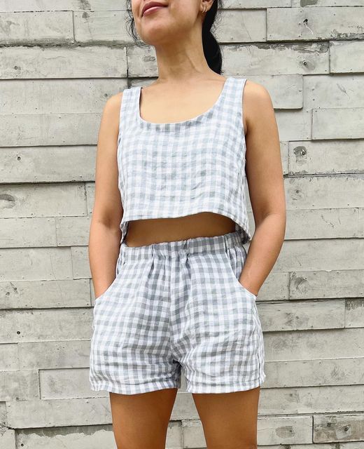 a woman standing in front of a brick wall wearing shorts and a cropped tank top