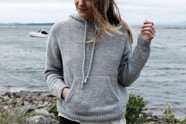 a woman standing by the water wearing a gray hoodie