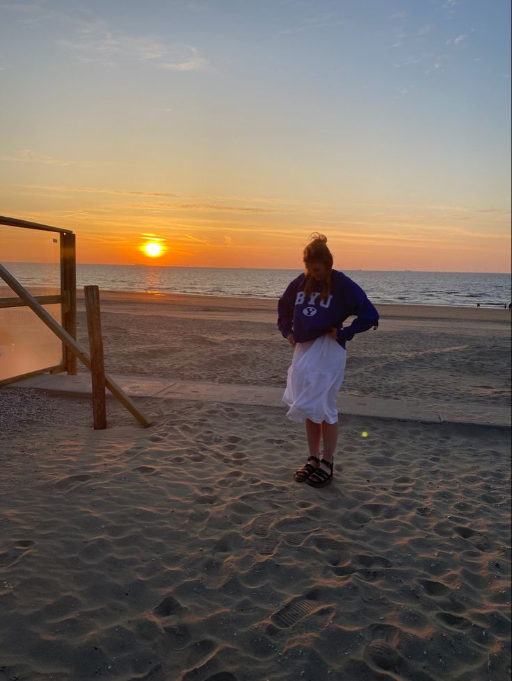 a man standing on top of a sandy beach next to the ocean at sun set