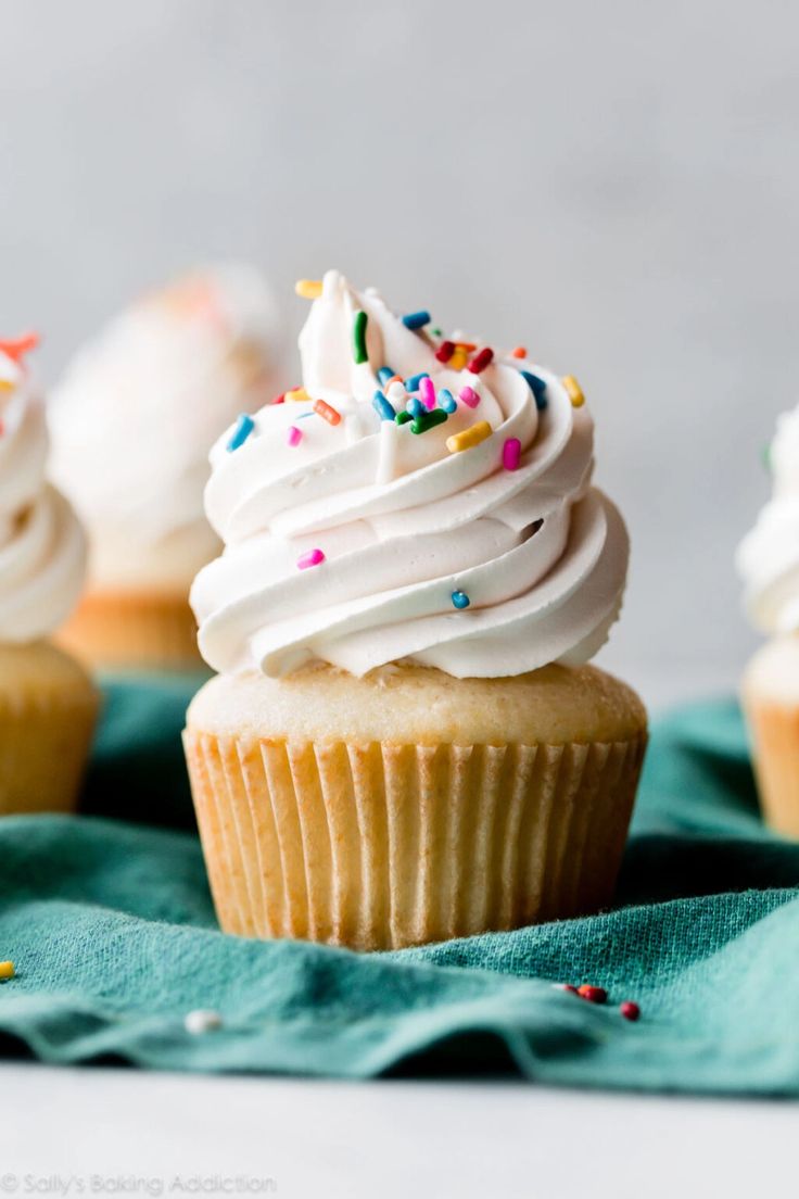 cupcakes with white frosting and sprinkles on a green napkin