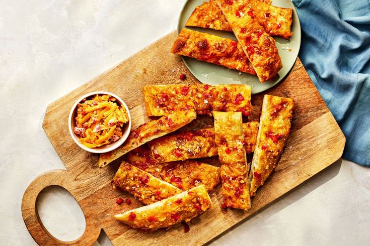 sliced pizza sitting on top of a wooden cutting board next to a bowl of sauce