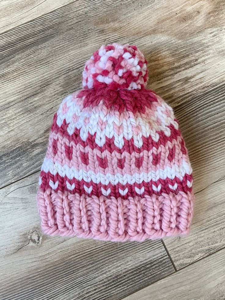 a pink and white knitted hat sitting on top of a wooden floor