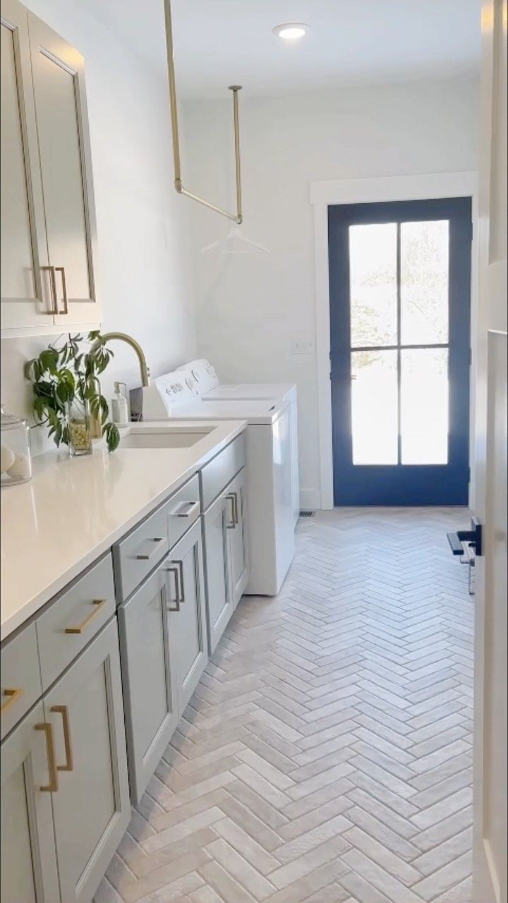 an empty kitchen with white cabinets and gray flooring is seen from the hallway leading to the front door