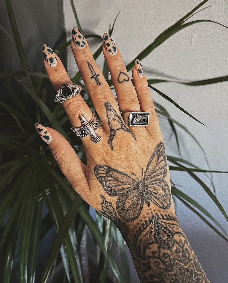 a woman's hand with tattoos and rings on her fingers, next to a potted plant