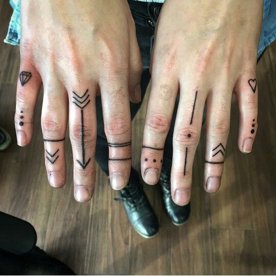 two fingers with different tattoos on them, one has an arrow and the other has a heart