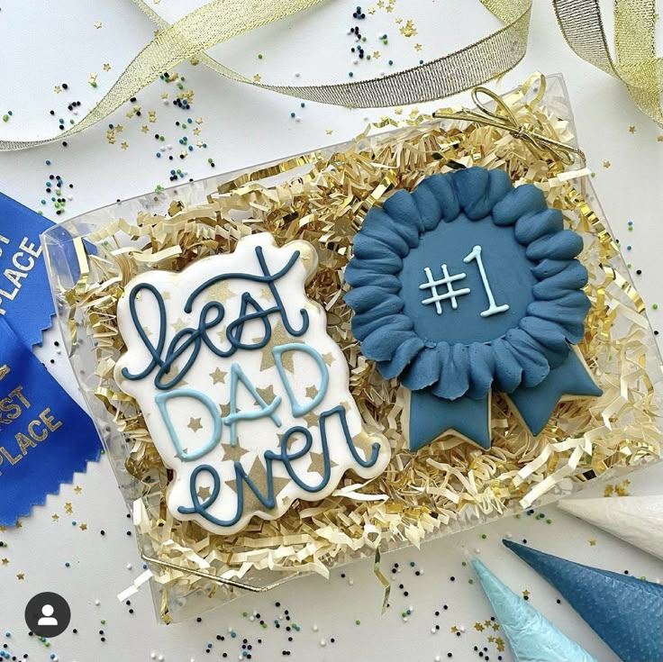 two decorated cookies in a gift box with blue ribbons and confetti on the table