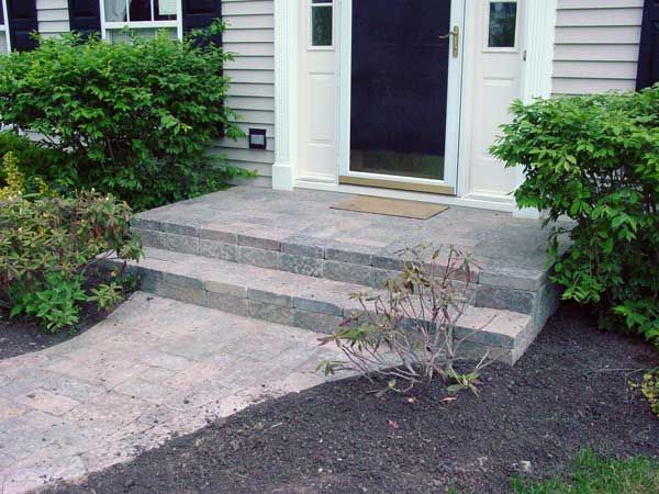 steps lead up to the front door of a house with bushes and shrubs around it