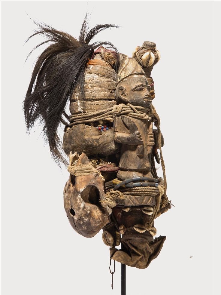 an old mask with feathers and other things on it's back end, hanging from a metal pole