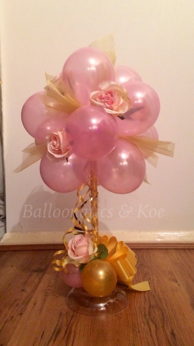 a vase filled with pink and gold balloons on top of a wooden floor next to a wall