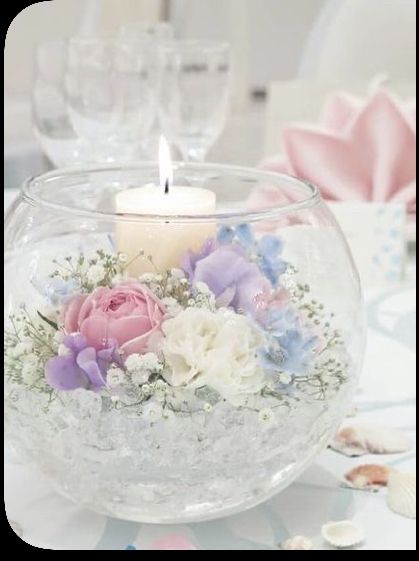 a glass bowl filled with flowers and a lit candle on top of a white table