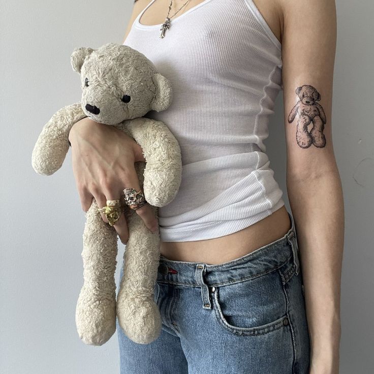 a woman holding a teddy bear in her right hand and tattoo on her left arm