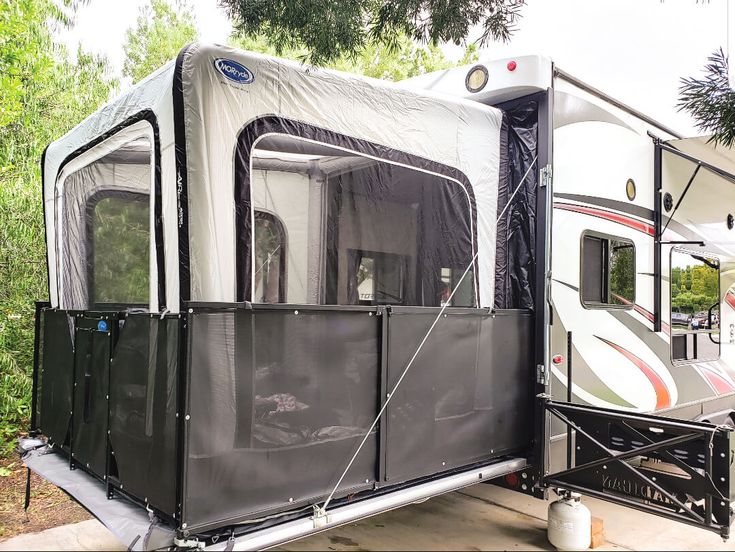 an rv parked on the side of a road next to trees and bushes with its awning closed