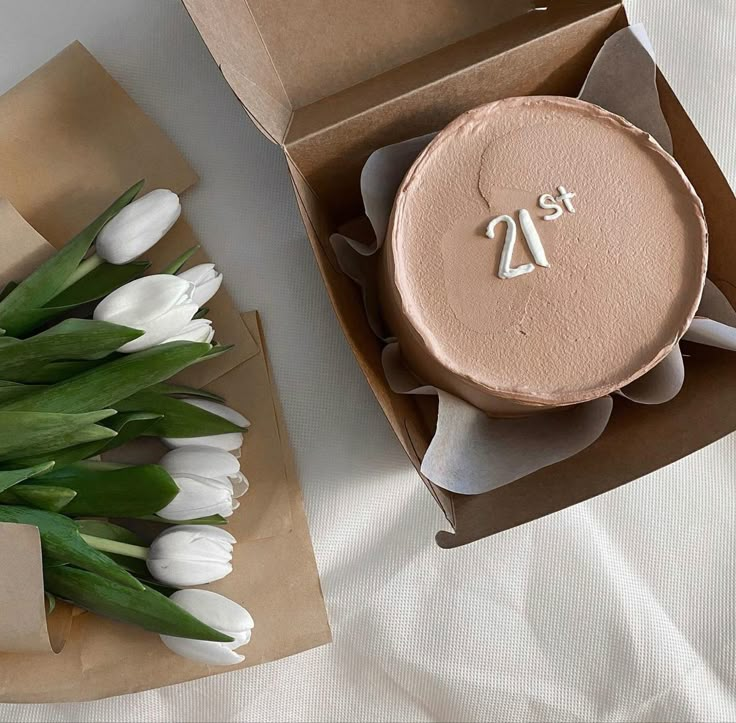 a cake with the number twenty on it in a box next to tulips