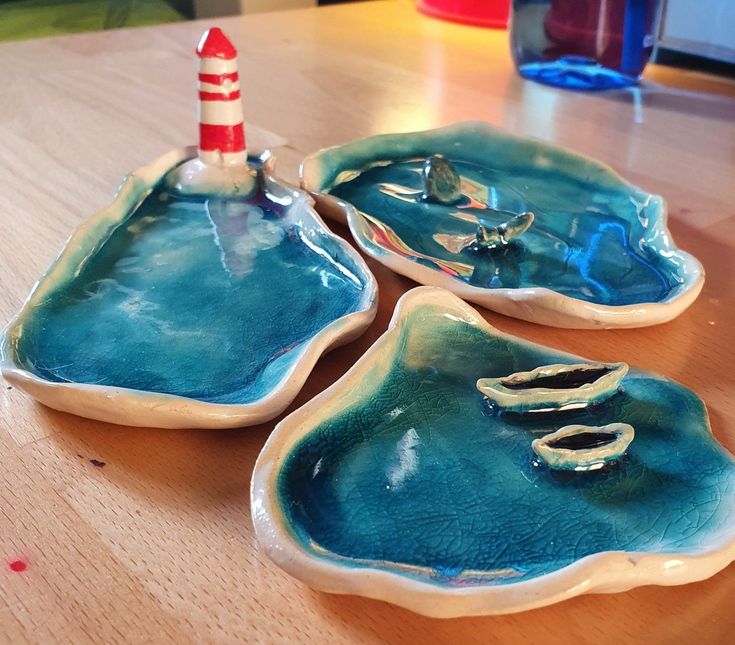 three blue dishes sitting on top of a wooden table next to a red and white lighthouse