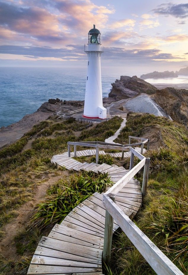 a white lighthouse on top of a hill next to the ocean with stairs leading up to it