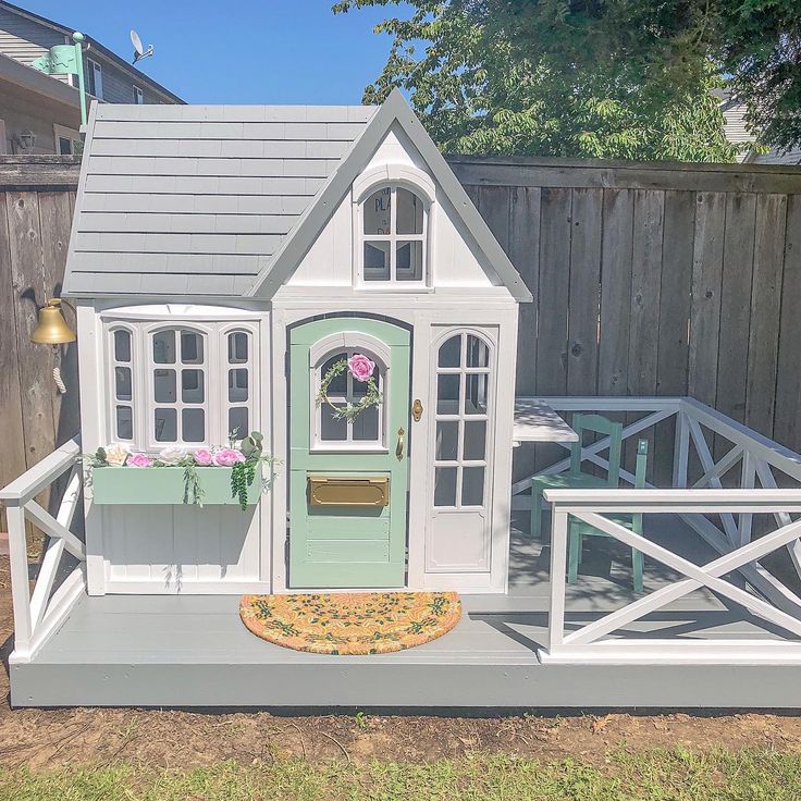 a doll house with a green door and windows on the outside, next to a fence