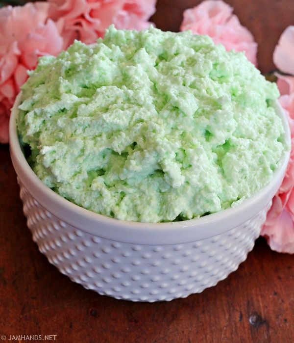 a white bowl filled with green frosting next to pink flowers on a wooden table