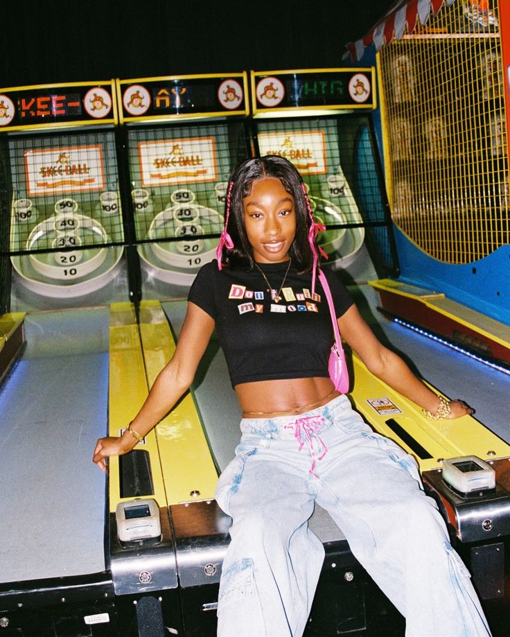 a woman sitting on top of a yellow and black pinball machine with headphones