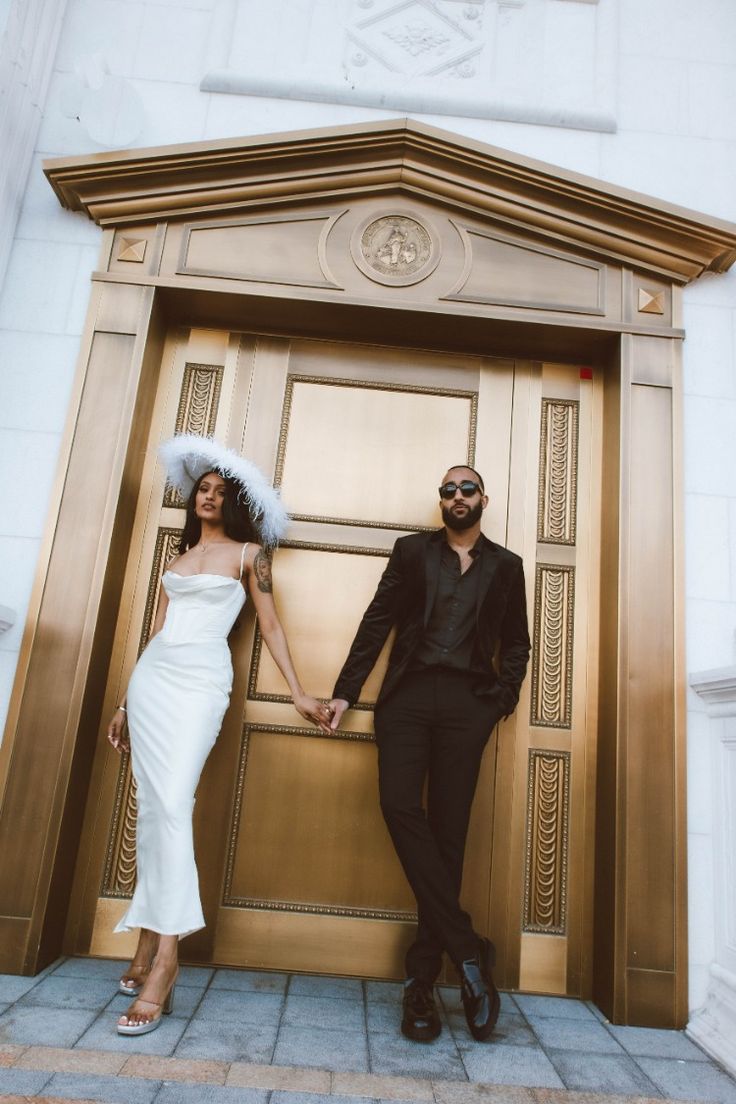 a man and woman holding hands while standing in front of an entrance to a building