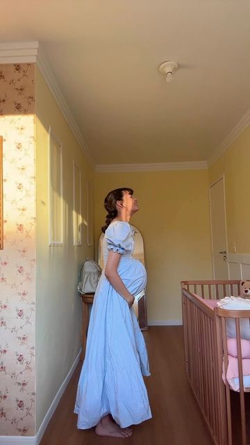 a woman in a blue dress is standing next to a crib and looking up