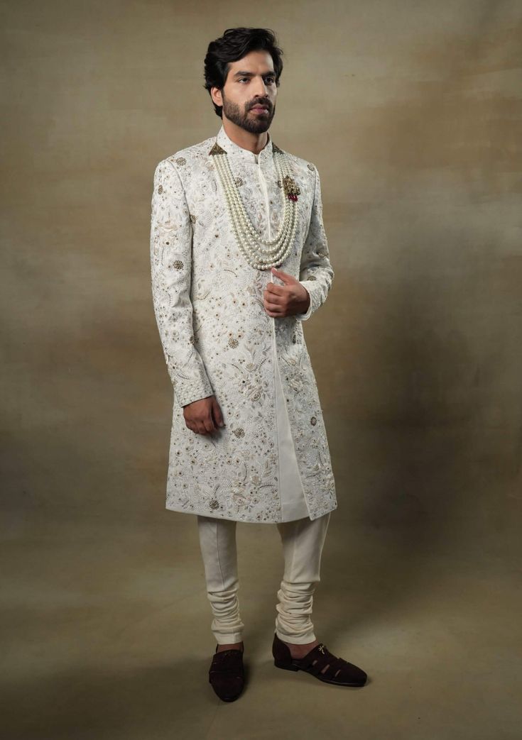 Editor's Note Featuring our work of art in our white all over hand-embroidered sherwani set. The foundation is crafted using machine embroidery adorned with tone on tone thread serving as the base texture, while the second tier showcases highlighting with 3D brass elements, dabka and zari threads. Fabric: Linen silk Color: Ivory, gold Components: Sherwani, kurta and churidar Occasion: Groom Fit: Regular Note: Product colour may slightly vary due to photographic lighting sources Care: Dry clean o Festive White Sets With Naqshi Detailing, Elegant Sherwani With Pearl Embroidery For Diwali, Embroidered Brocade Sherwani For Reception, Festive White Set With Naqshi Details, Traditional Brocade Sherwani With Gold Embroidery, Festive Off-white Sets With Naqshi, Pearl Embroidered Nehru Jacket For Wedding And Eid, Elegant Raw Silk Sherwani With Gold Embroidery, Ceremonial Brocade Sherwani With Intricate Embroidery