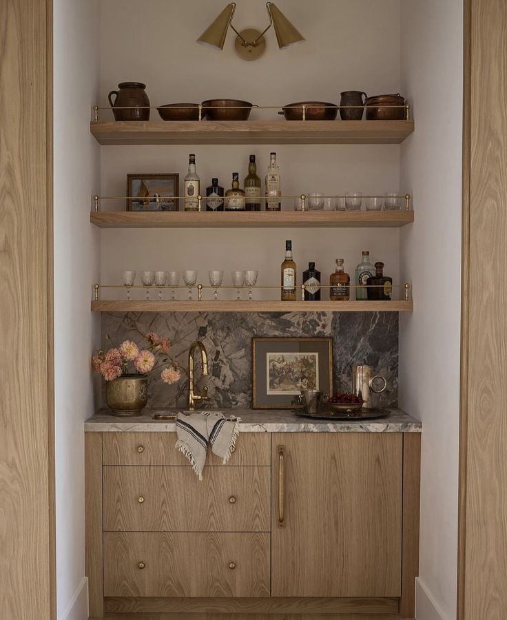 the shelves in this kitchen are filled with bottles and glasses on top of marble counter tops