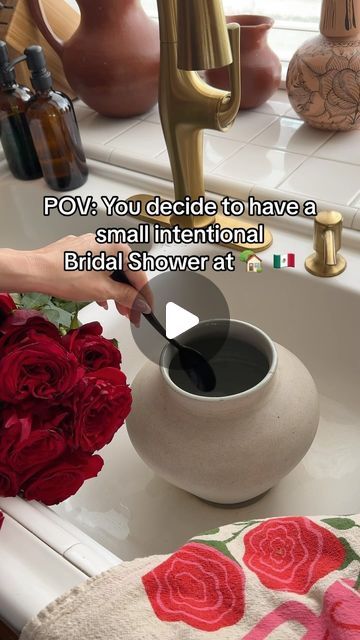 a woman is pouring black liquid into a bowl with roses in the sink next to it