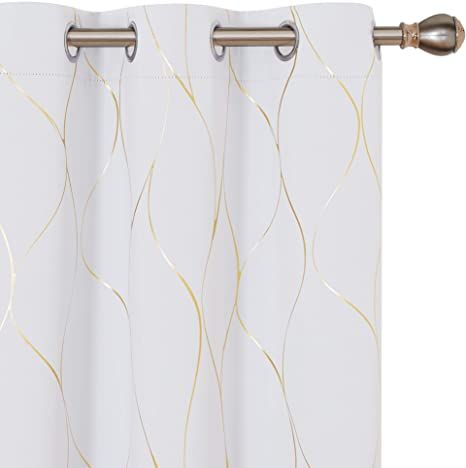 a white curtain with gold swirls on the top and bottom, hanging from a metal rod