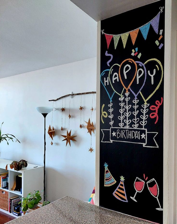 a birthday chalkboard with balloons and confetti hanging from it's side