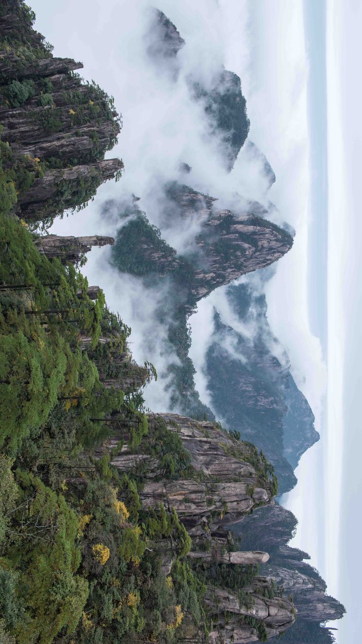 the mountains are covered in thick clouds and trees on either side of the river or lake