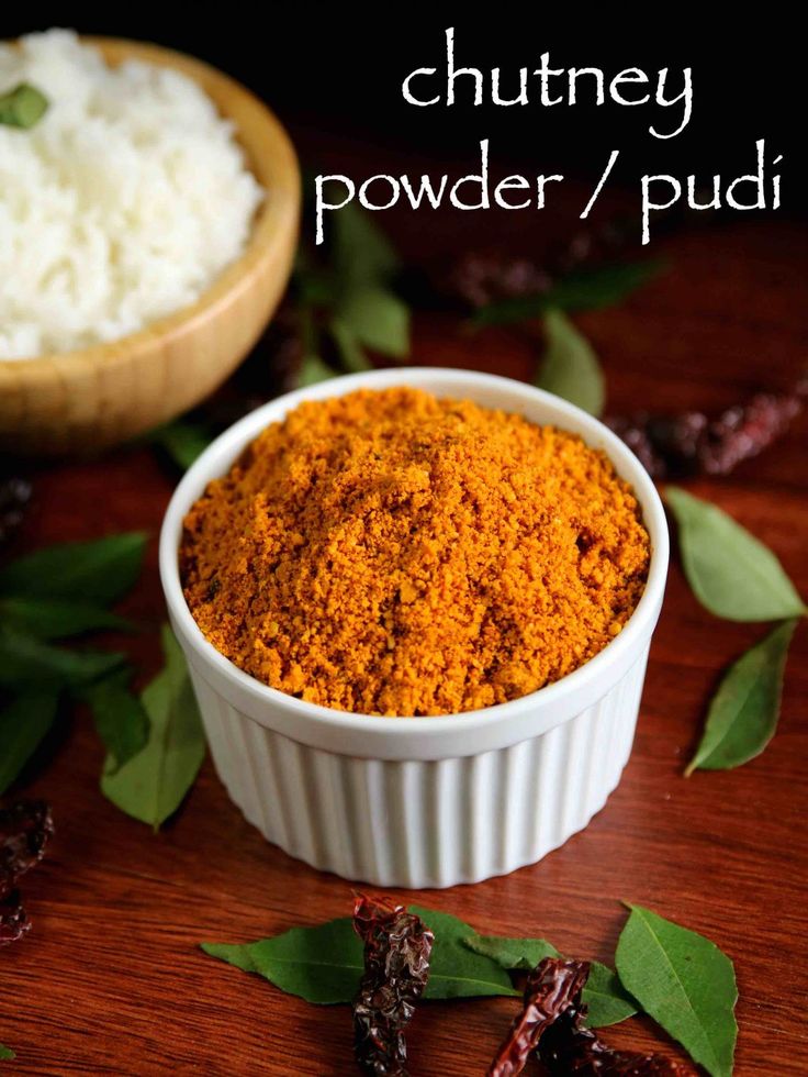 a bowl filled with powder next to some leaves and spices on a wooden table top