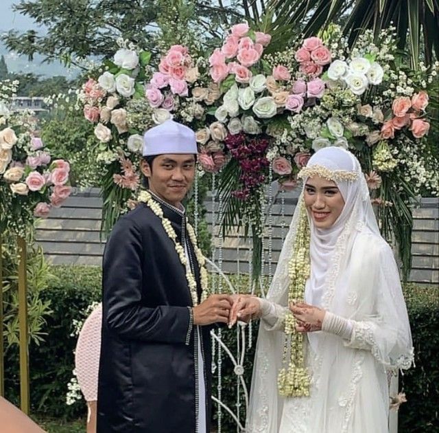 a man and woman standing next to each other in front of a flower covered archway