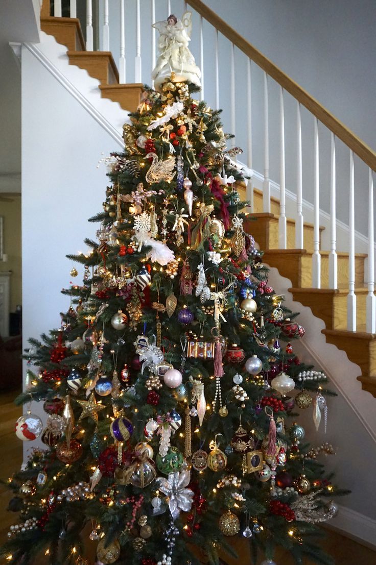 a christmas tree with ornaments on it in front of a stair case and banister