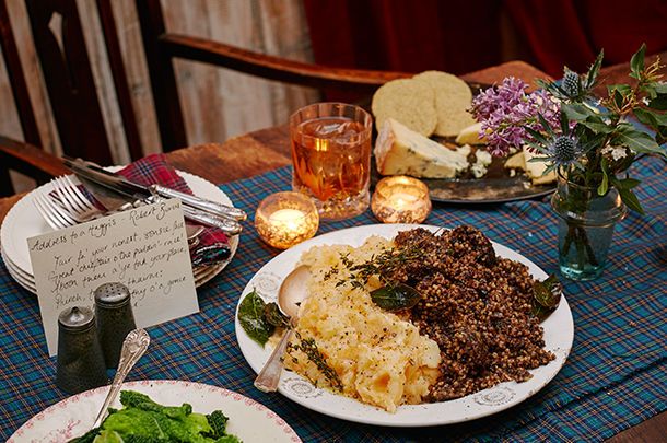 a table topped with plates of food next to glasses and flowers on top of a wooden table