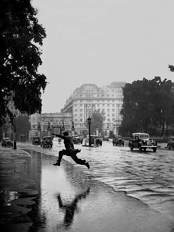 a person jumping in the air while holding an umbrella on a rainy day with cars and buildings in the background