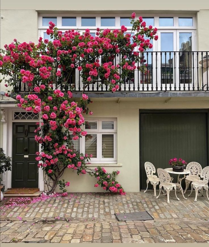 pink flowers are growing on the side of a building with white chairs and tables outside