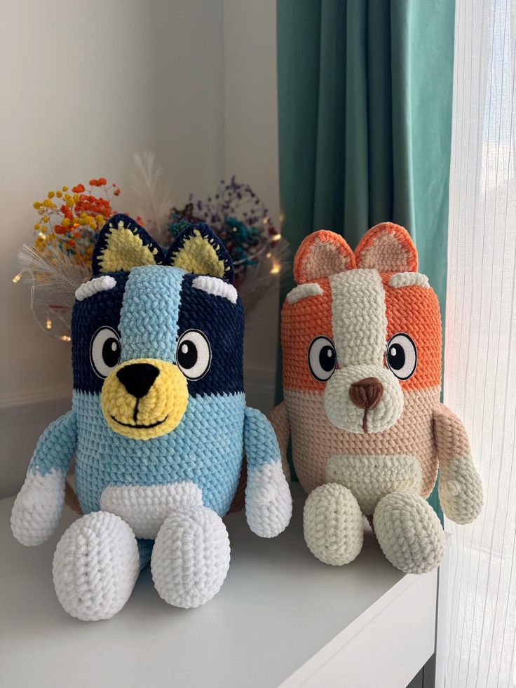 two crocheted stuffed animals sitting next to each other on a shelf in front of a window