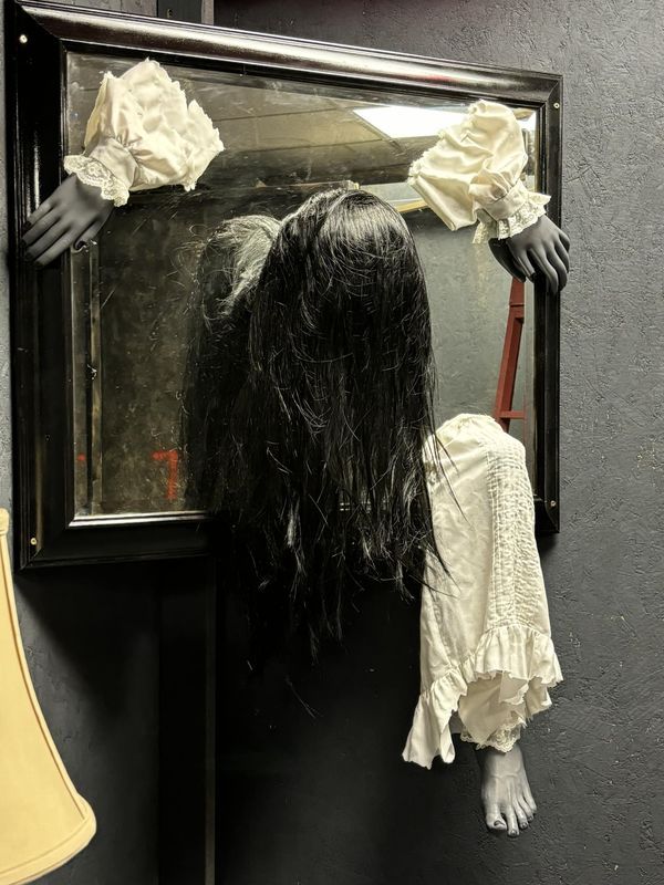 a creepy doll is standing in front of a mirror with her hands on the door handle