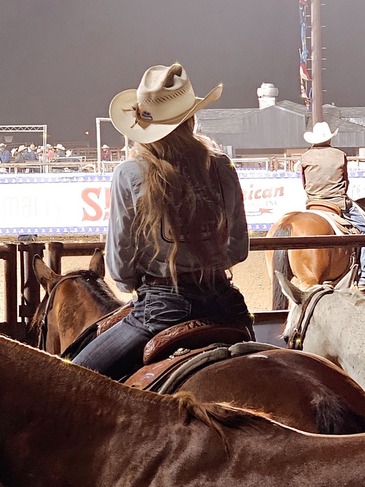 a woman wearing a cowboy hat riding on the back of a brown horse in an arena