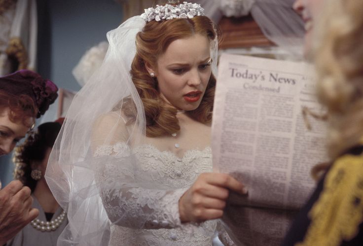 a woman in a wedding dress reading a newspaper while wearing a tiara and veil