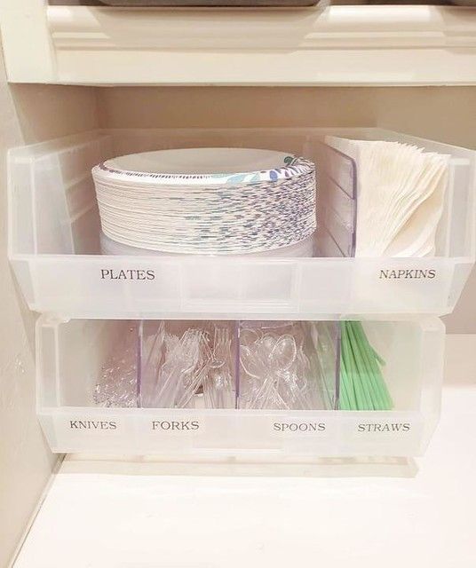 plastic storage bins filled with various items in a kitchen cabinet, labeled plates, napkins and spoons