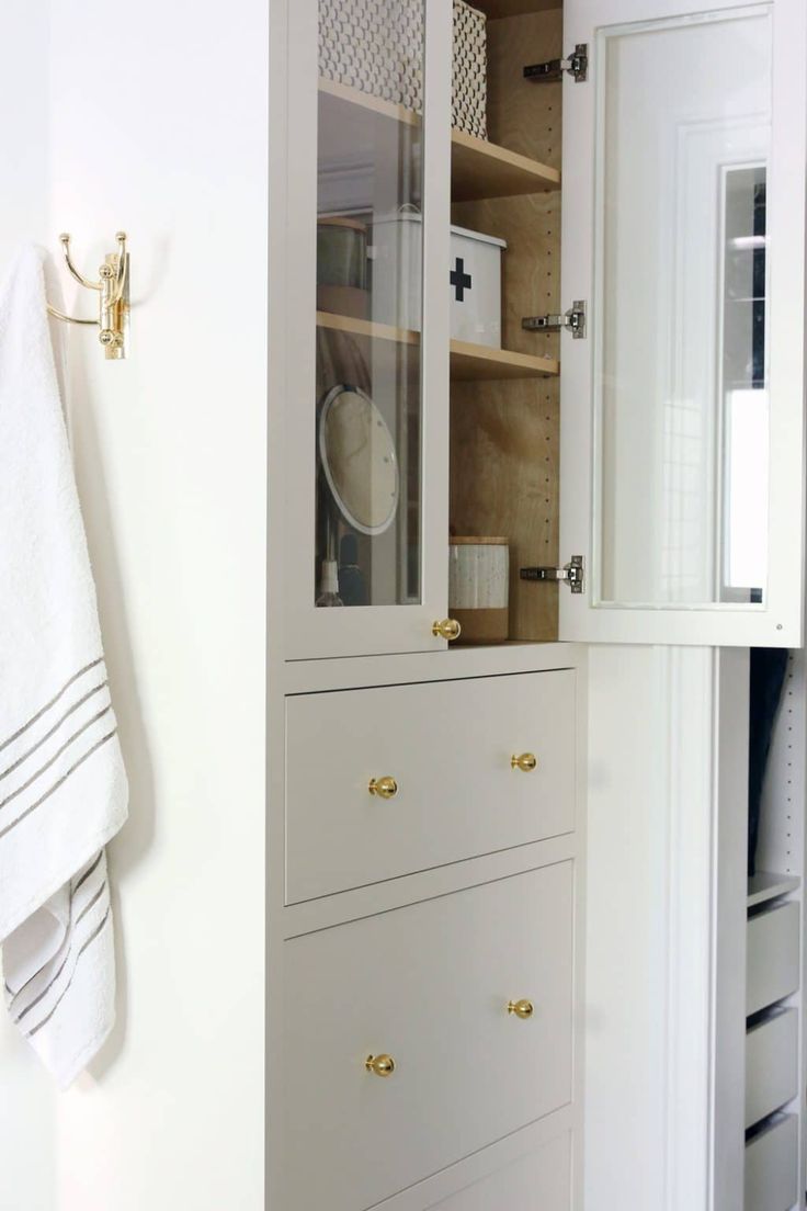 a white cabinet with glass doors and drawers in a bathroom next to a towel rack