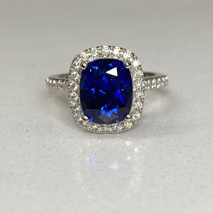 "The ring pictured is a lab created blue sapphire with moissanite accents #6813 Shown in 14k white gold and 14k yellow gold This ring is also offered with diamond accents Use the drop down menu to make your selection instagram: https://www.instagram.com/p/BurdXxKlTZd/ -Approximate total carat weight: 3.00ctw diamond equivalent -Center Stone Size: 9x7mm - approx. 2.60ct diamond equivalent -Center Stone Shape: elongated cushion -Gem Type: lab created sapphire -Stone Clarity: VS2 -Stone Color: Blue Sapphire Cushion Cut Ring With Center Stone, Sapphire Diamond Ring With Prong Setting Cushion Cut, Lab-created Sapphire Diamond Ring In Cushion Cut, Blue Lab-created Sapphire Diamond Ring With Accent Stones, Cushion Cut Sapphire Ring With Cubic Zirconia Accent Stones, Blue Sapphire Radiant Cut Promise Ring, Cushion Cut Diamond Ring With Center Stone Lab-created Sapphire, Sapphire Wedding Ring With Brilliant Cushion Cut, Blue Radiant Cut Sapphire Promise Ring