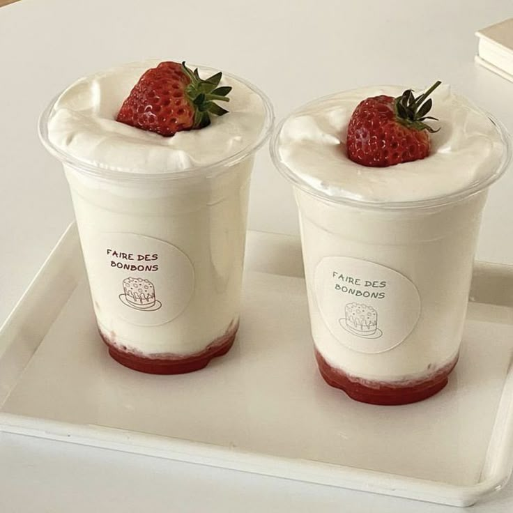 two yogurt cups with strawberries on top are sitting on a white tray