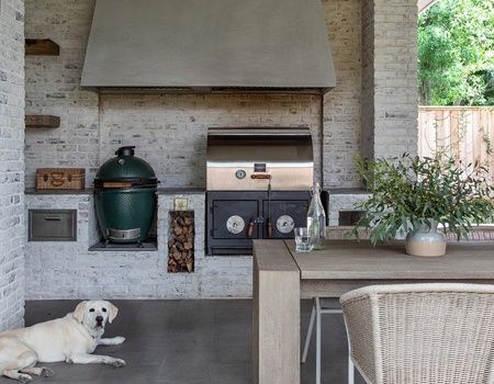 a white dog laying on the floor in front of an outdoor kitchen with a grill